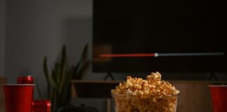 tavolino con bibite e popcorn, sullo sfondo una tv che proietta un film