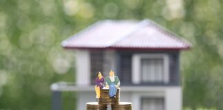 Coppia di figurine umane stilizzate sedute su una pila di monete. sullo sfondo una casa